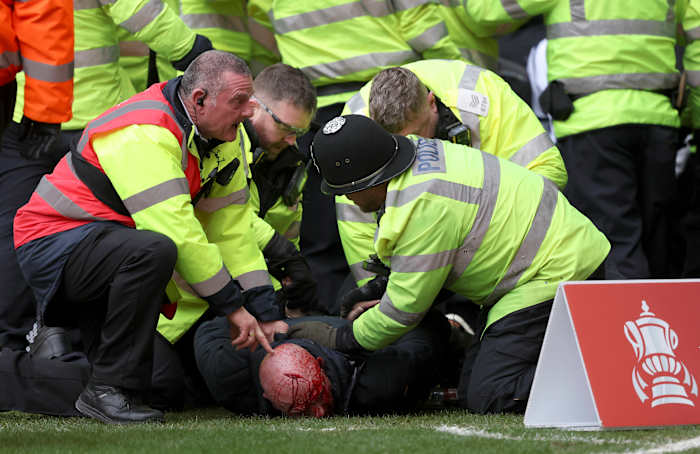 Police officers and a security steward pictured restraining an injured fan following crowd violence during an FA Cup game between West Brom and Wolves in January 2024